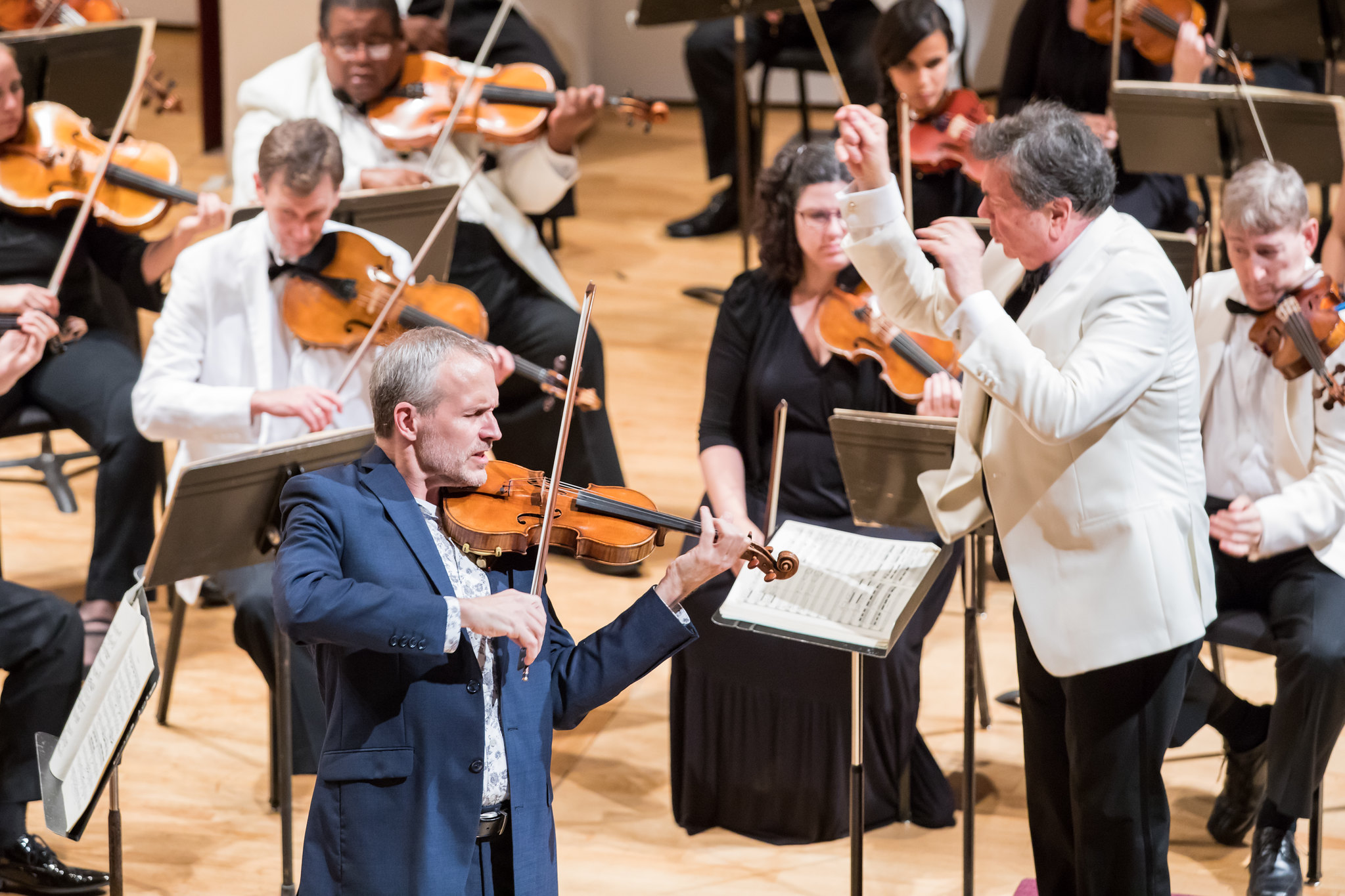 Violinist Jeff Multer in blue jacket performing music with Eastern Festival Orchestra led by conductor Gerard Schwarz