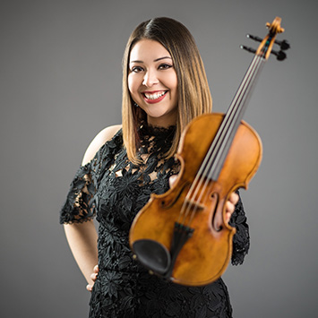 woman in studio lighting smiling at camera and holding violin
