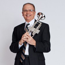white man in suit with white studio background holding a trumpet