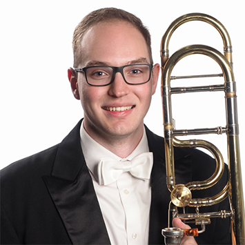 3/4 portrait headshot of Steven in a tux and white tie, holding his trombone against his left shoulder. The background is a portrait solid white.